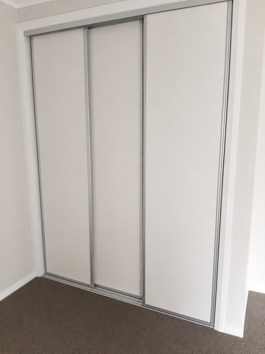 Bedroom wardrobe with white sliding doors in aluminium frames - Ambient Civil Auckland
