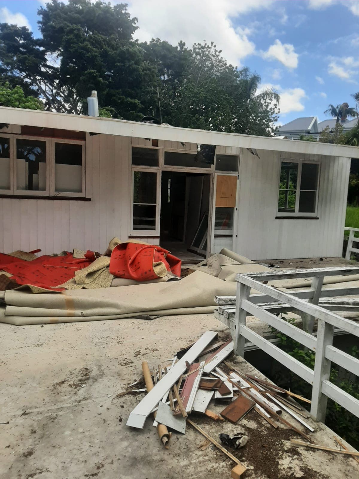 Weatherboard house stripped out during demolition with carpet rolls and timber debris piled outside - Ambient Civil Auckland