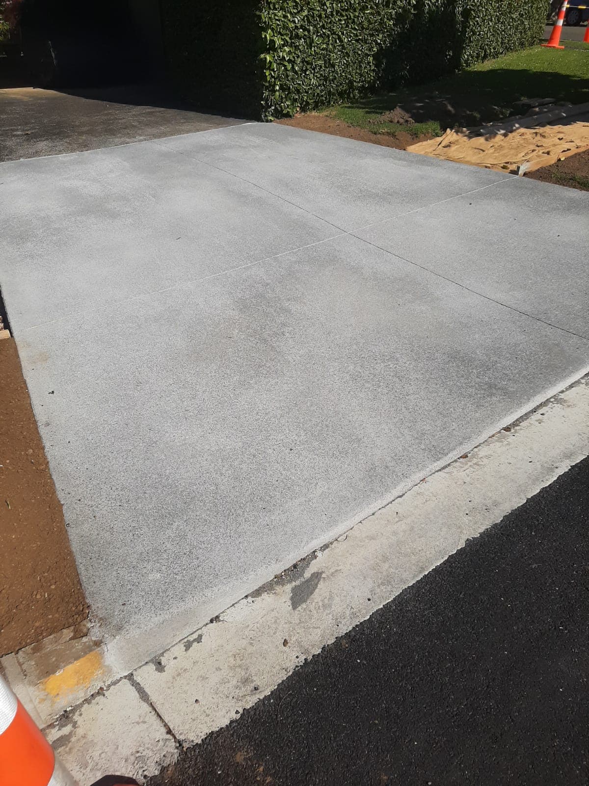Newly poured concrete driveway section meeting the road edge with hedge border - Ambient Civil Auckland