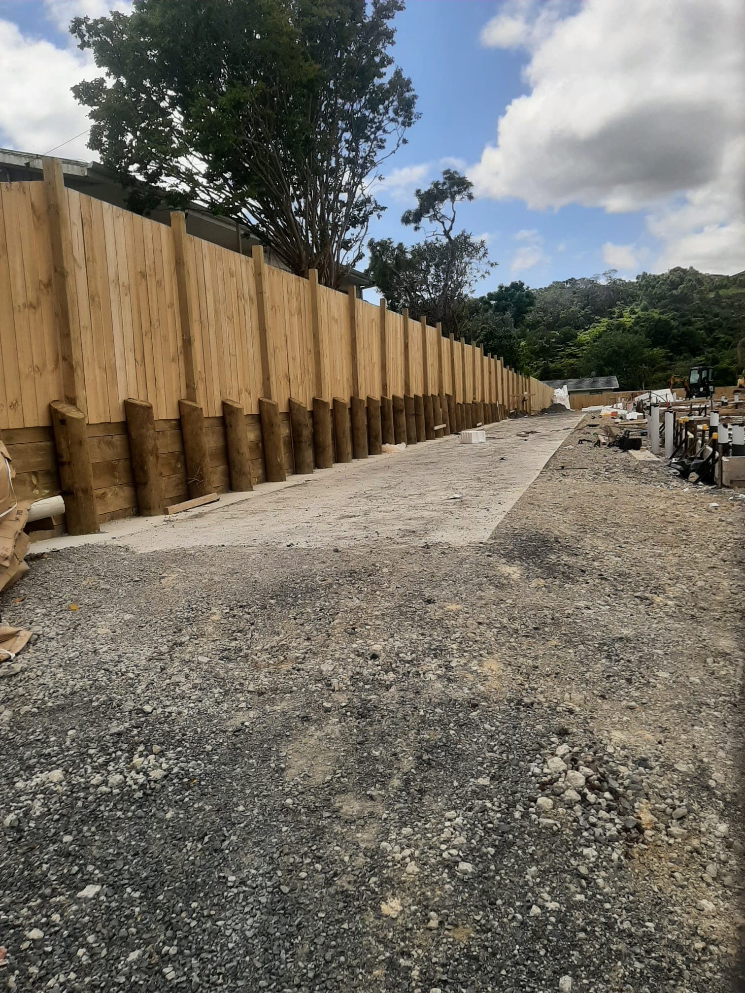 Completed timber pole retaining wall with fence beside a gravel access driveway - Ambient Civil Auckland