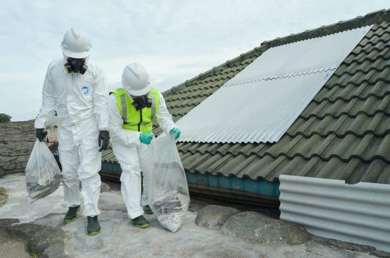 Workers in hazmat suits removing bagged asbestos sheeting from a roof - Ambient Civil Auckland