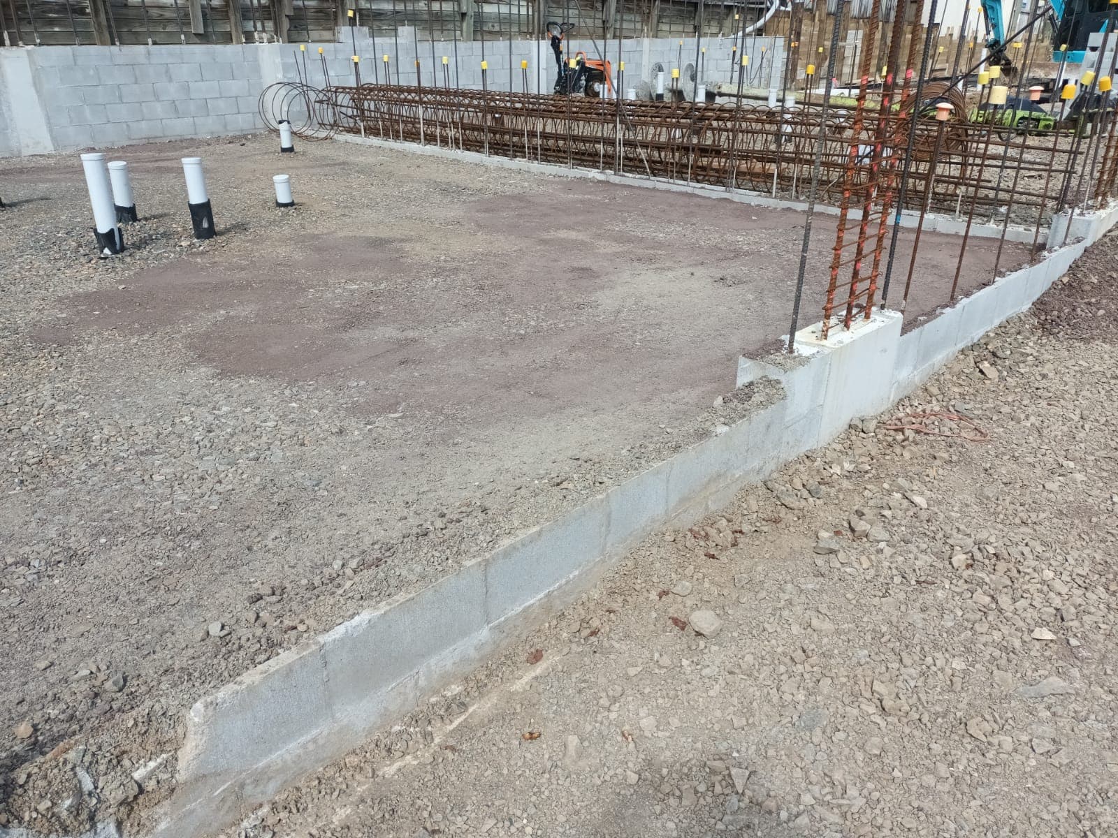 Poured concrete foundation footing with rebar columns and excavator on a building site - Ambient Civil Auckland