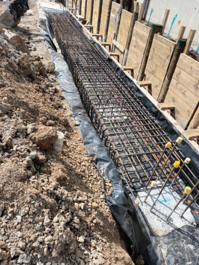 Reinforced footing trench with rebar cage and membrane beside timber retaining wall - Ambient Civil Auckland