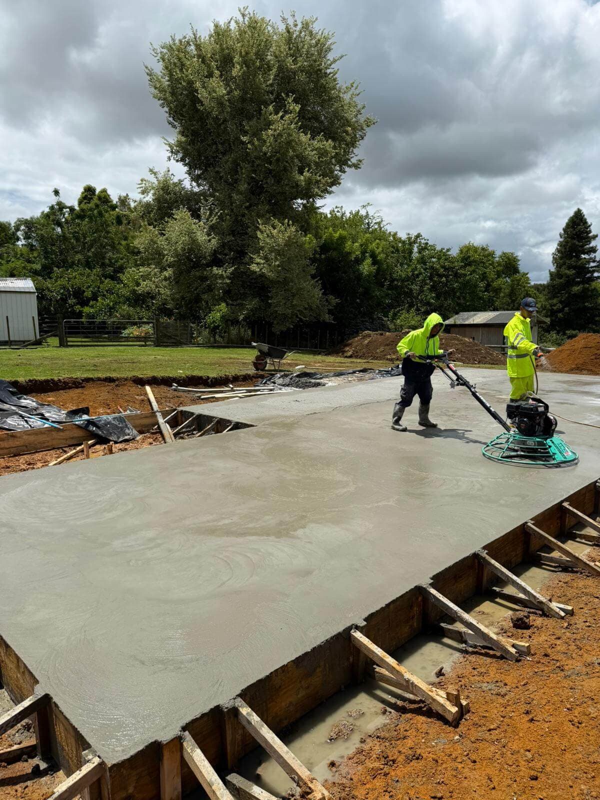 Workers power-floating a freshly poured concrete slab in timber formwork - Ambient Civil Auckland