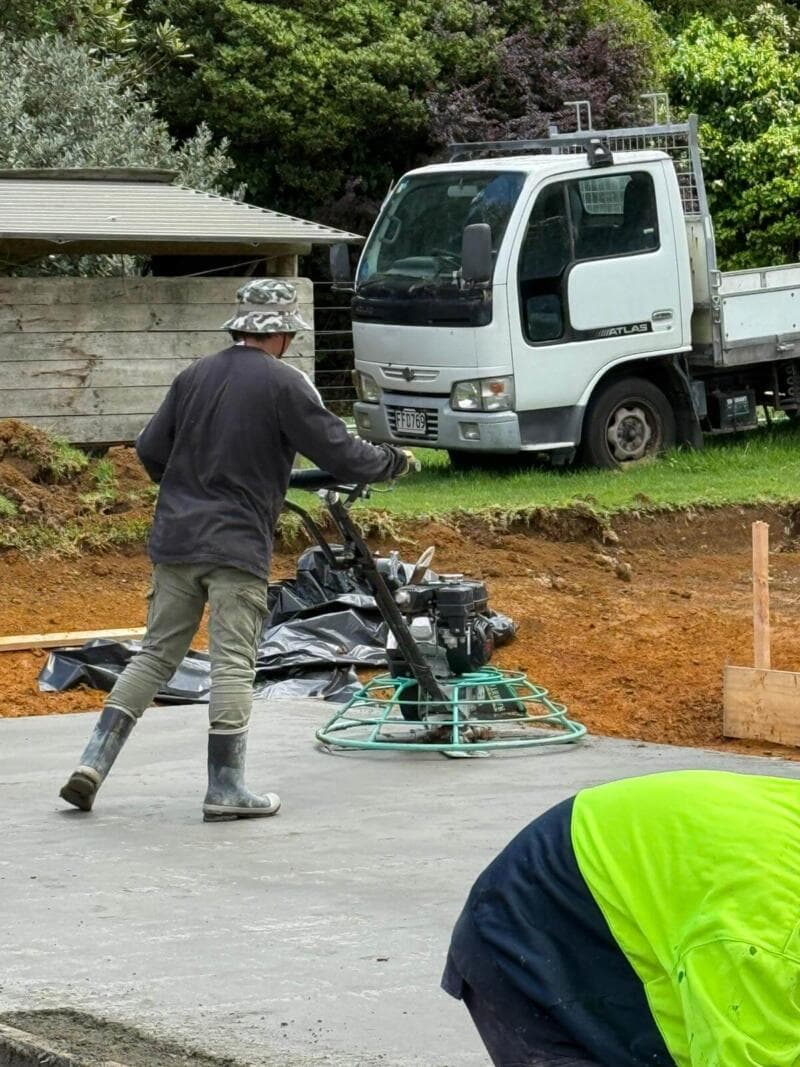 Worker finishing a fresh concrete slab with a power trowel on a residential build - Ambient Civil Auckland