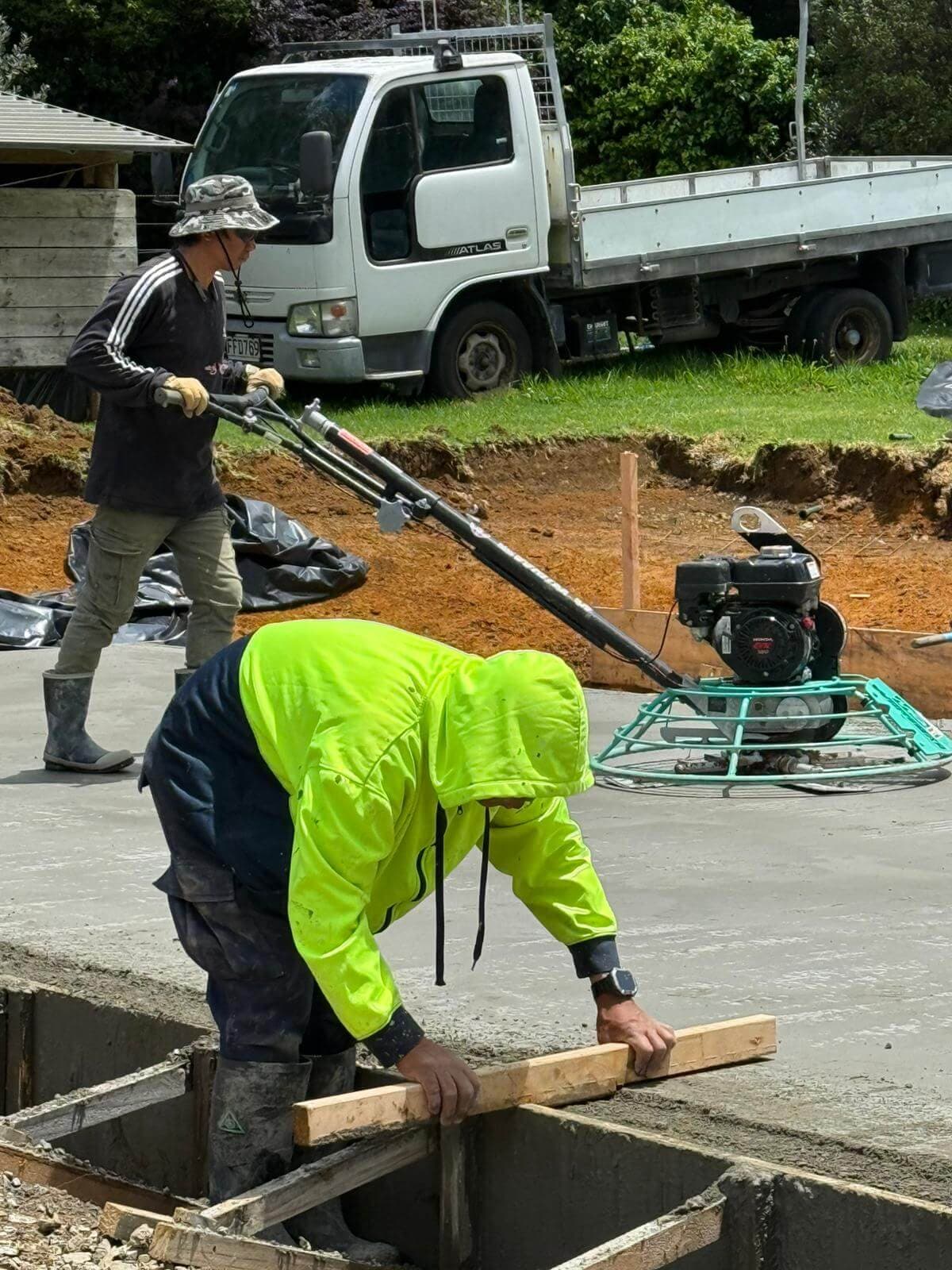 Worker screeding a wet concrete slab while finishing with a power trowel - Ambient Civil Auckland