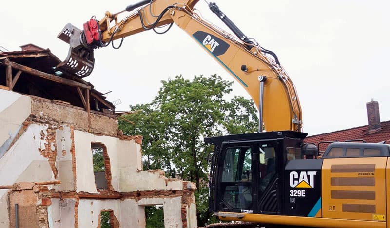 CAT excavator with demolition grapple tearing down a brick building - Ambient Civil Auckland