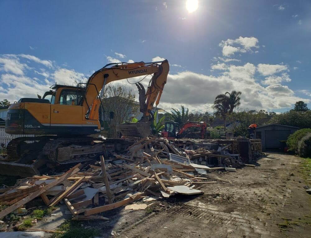 Hyundai excavator demolishing a house amid timber rubble on an Auckland site - Ambient Civil Auckland