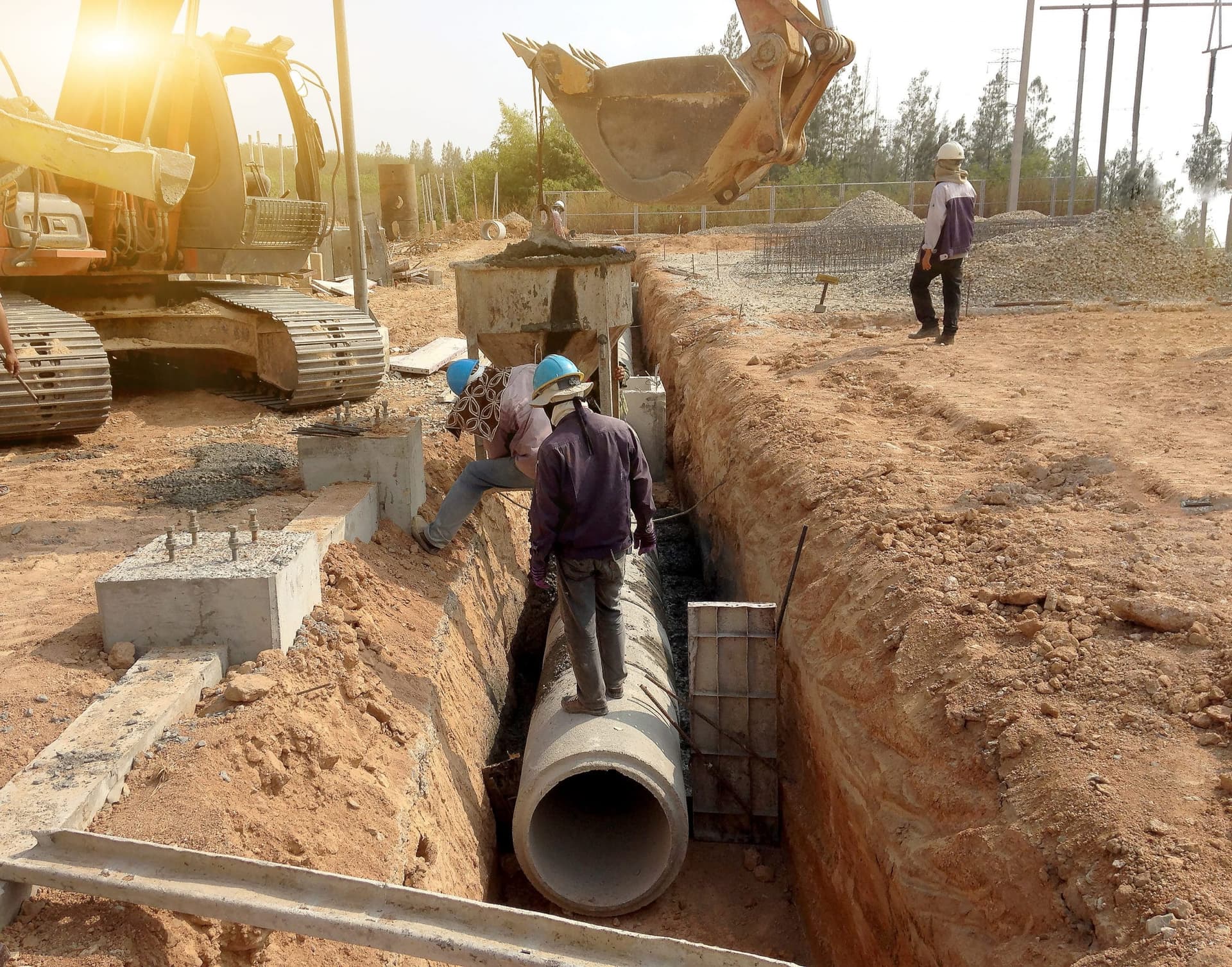 Excavator and workers installing concrete drainage pipe in trench - Ambient Civil Auckland