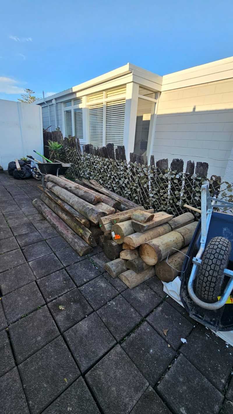 Timber retaining wall poles staged on a paved residential site before installation - Ambient Civil Auckland