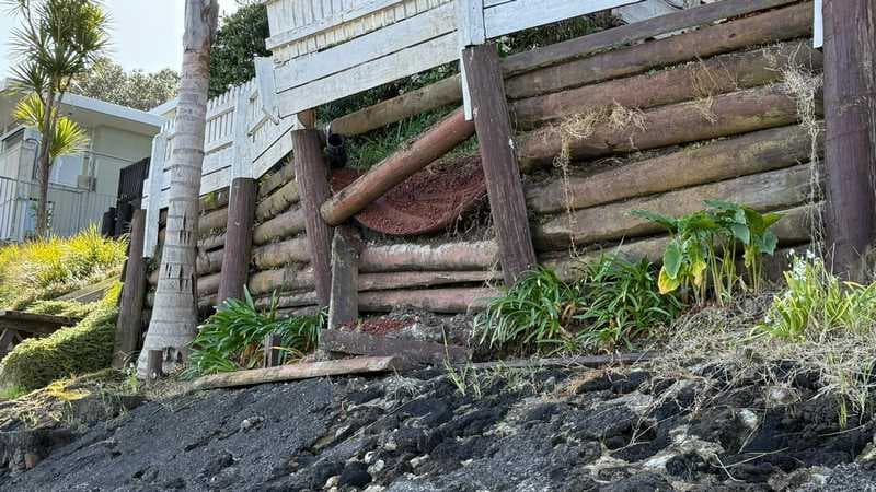 Timber log retaining wall with exposed drainage pipe and eroded fill on a slope - Ambient Civil Auckland