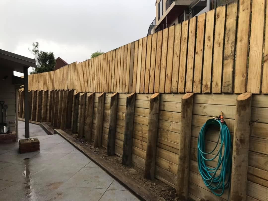 Timber pole retaining wall topped with paling fence beside concrete path - Ambient Civil Auckland
