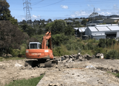 Orange excavator carrying out earthworks on a rocky Auckland site - Ambient Civil Auckland