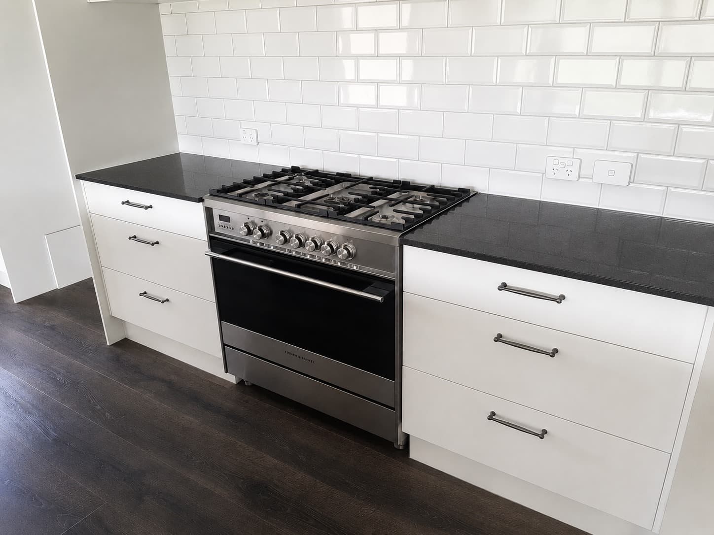 Renovated kitchen with stainless range black benchtop and white cabinetry - Ambient Civil Auckland