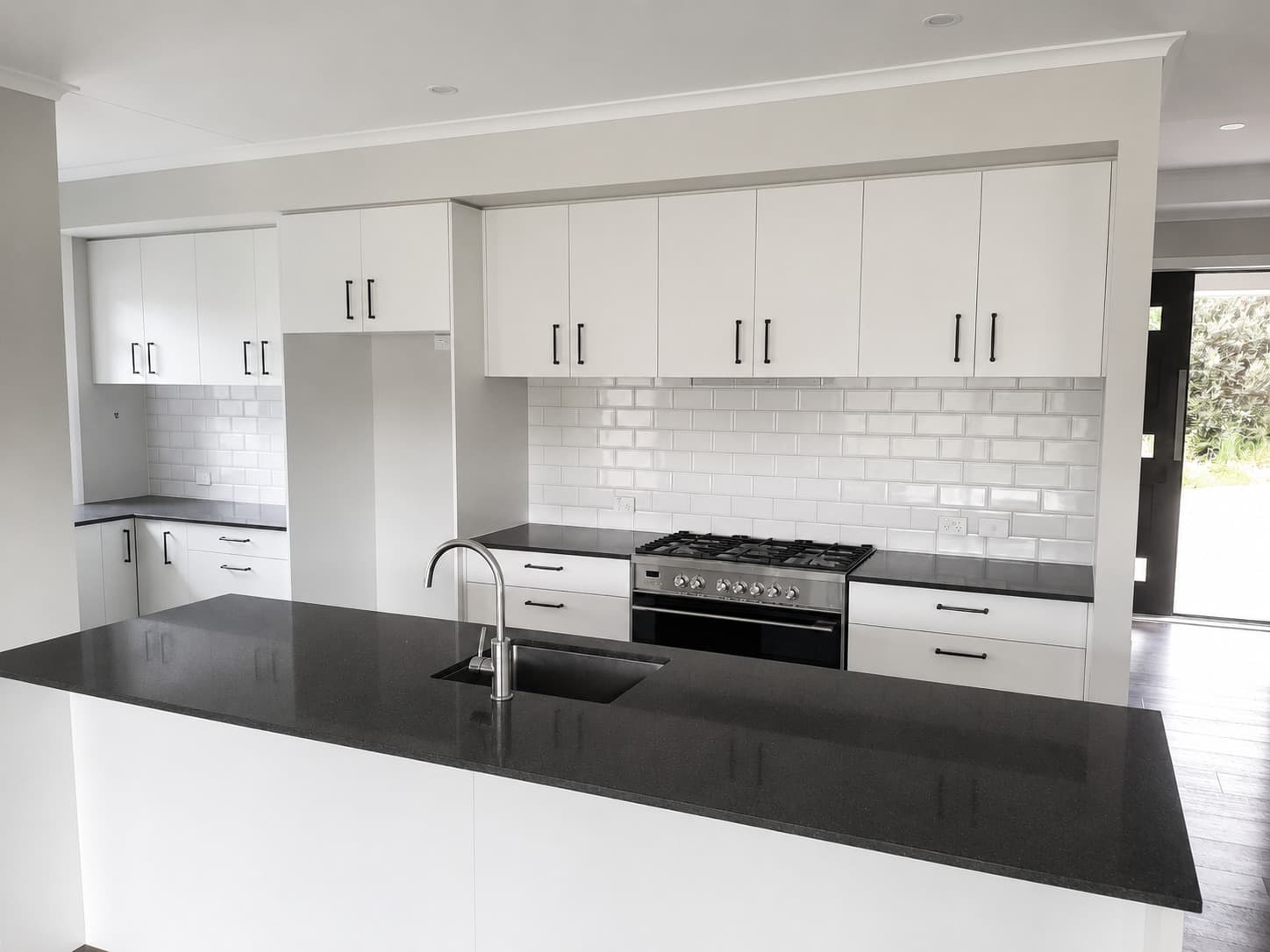 Wide view of renovated open-plan kitchen with white cabinetry and black benchtops - Ambient Civil Auckland
