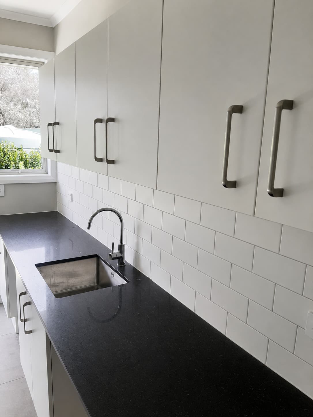 Renovated laundry with stainless sink black benchtop and subway tile splashback - Ambient Civil Auckland