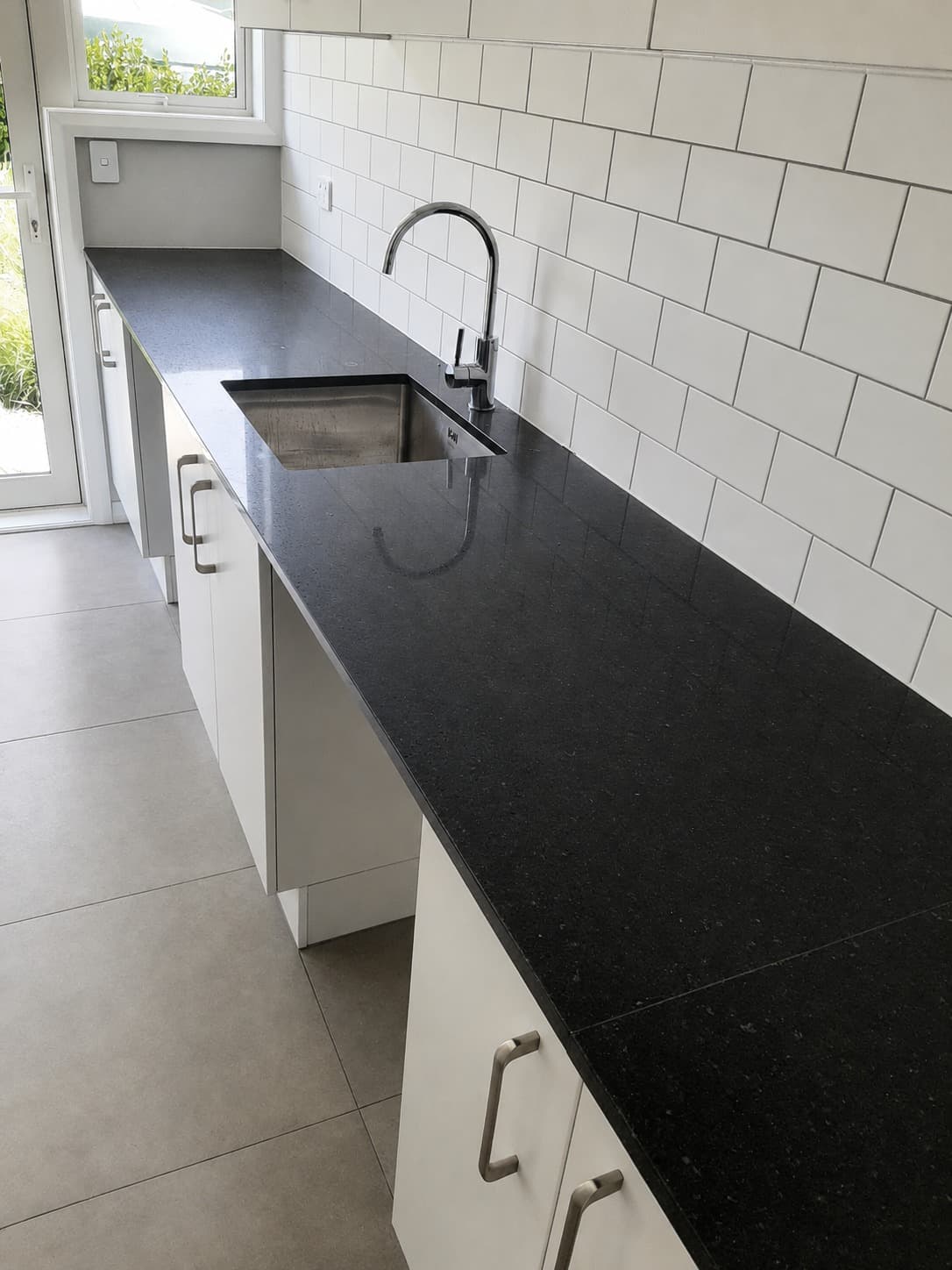 Renovated laundry with black stone benchtop, undermount sink and subway tile wall - Ambient Civil Auckland