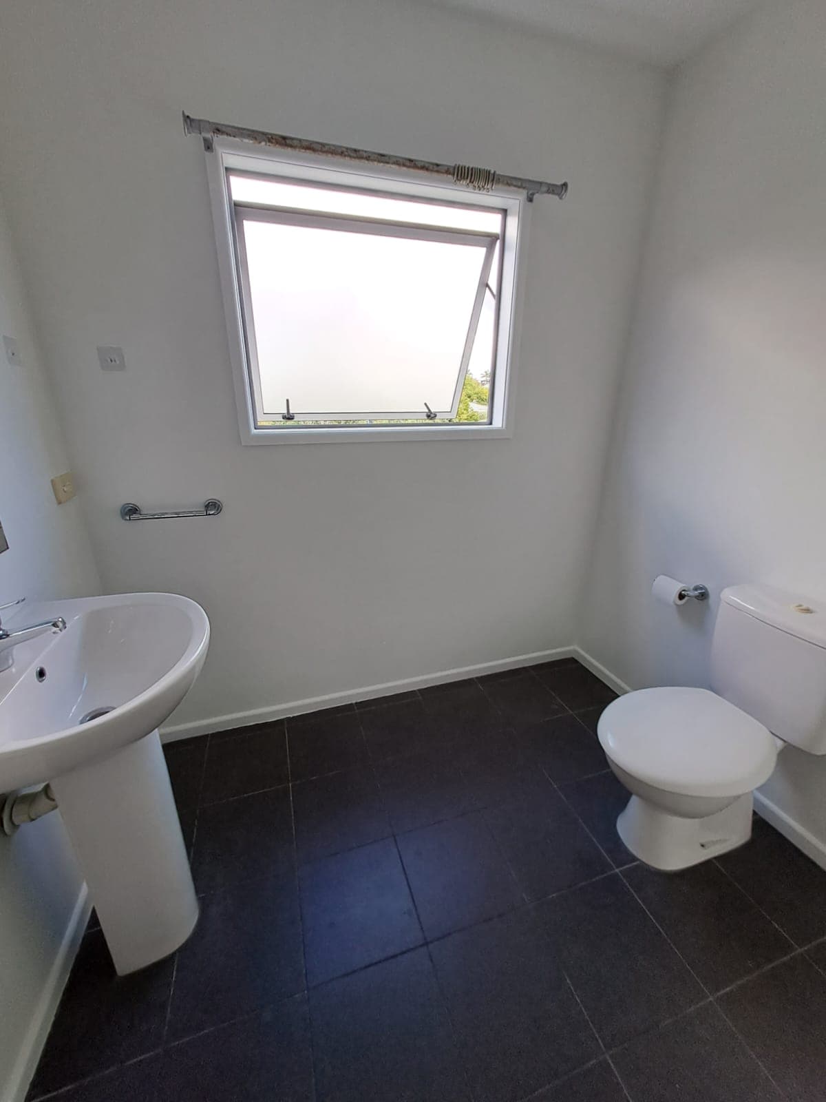 Finished bathroom with pedestal basin toilet and freshly painted white walls and tiled floor - Ambient Civil Auckland