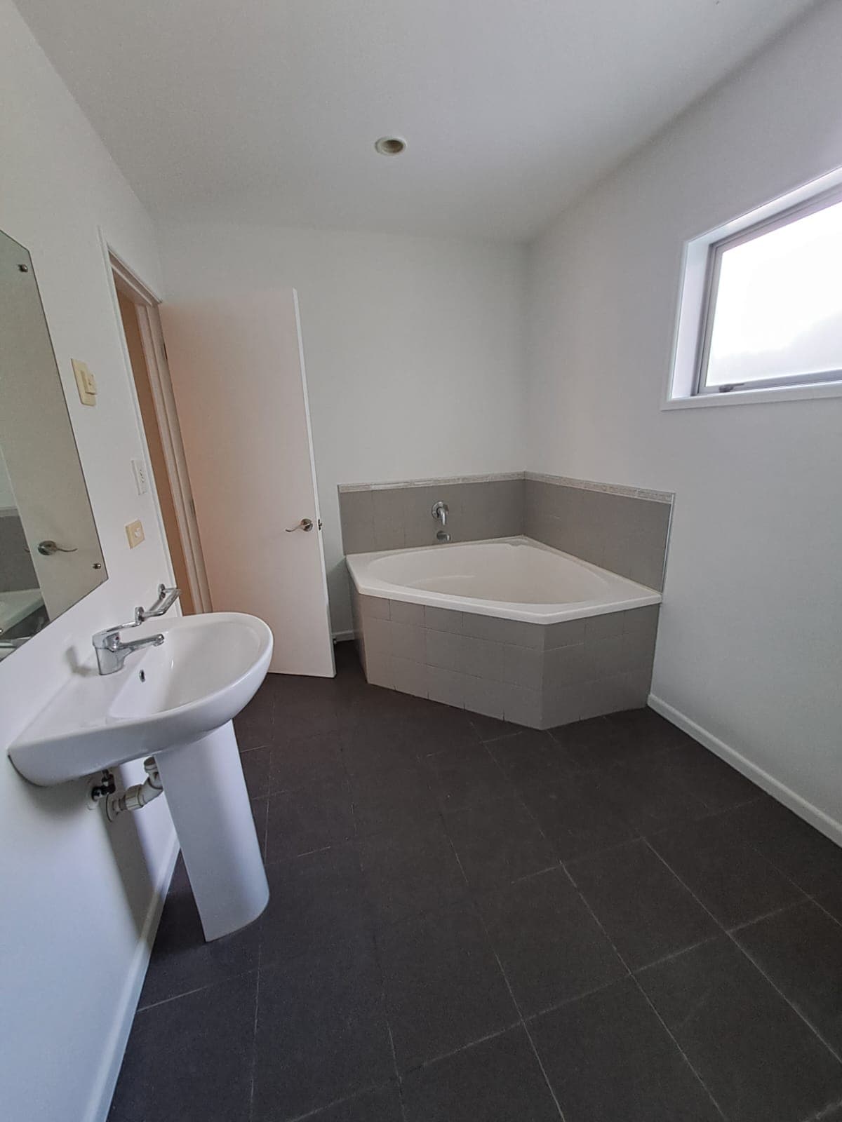 Finished bathroom with tiled corner bathtub pedestal basin and freshly painted walls - Ambient Civil Auckland