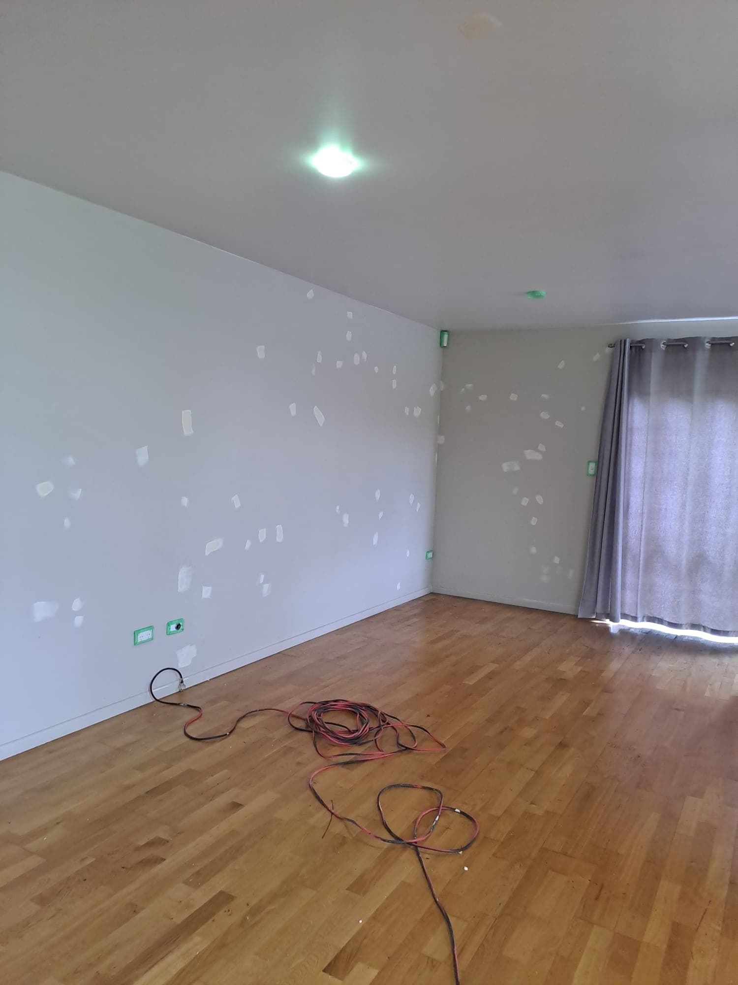 Living room with patched walls and timber floor mid-repaint with extension cords on floor - Ambient Civil Auckland